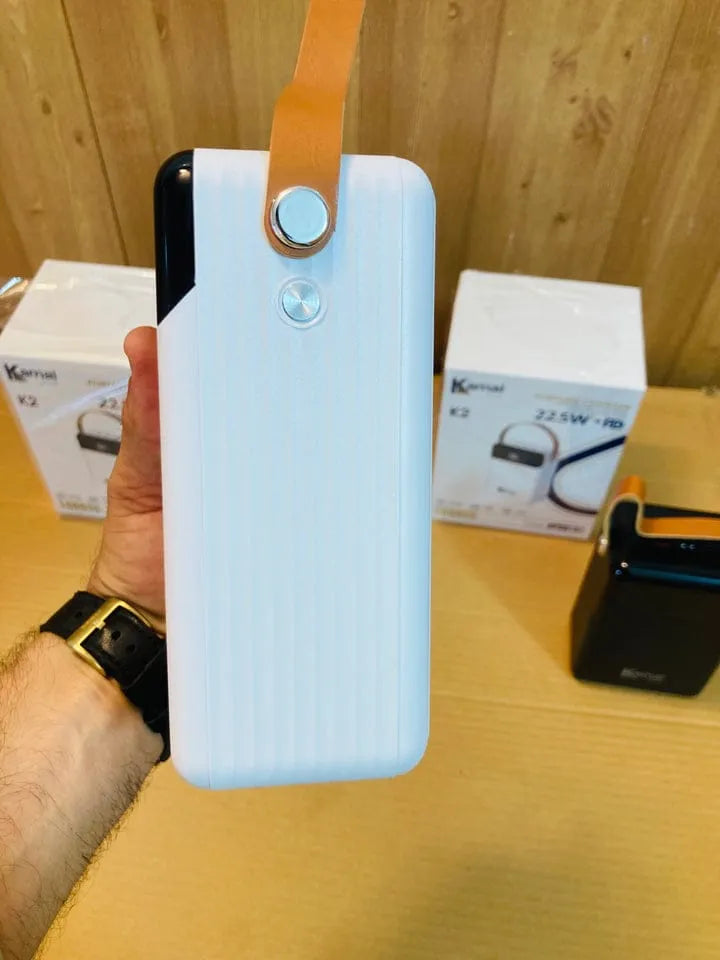 Hand holding a white power bank with a strap against a wooden background