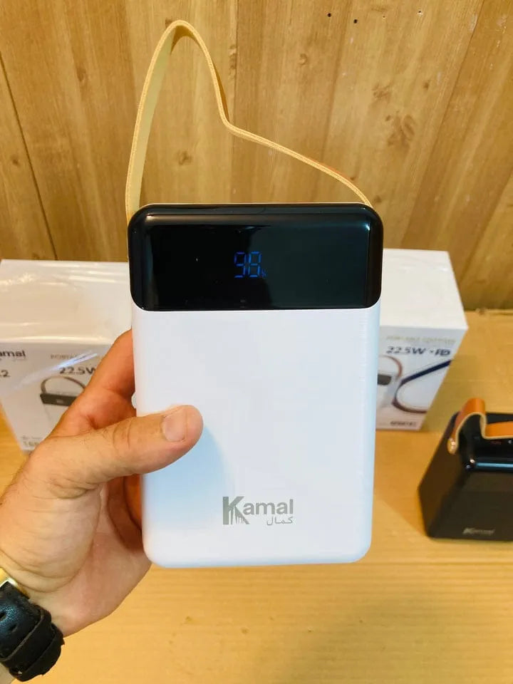 Hand holding a white power bank with a black top labeled 'Kamal' against a wooden background.