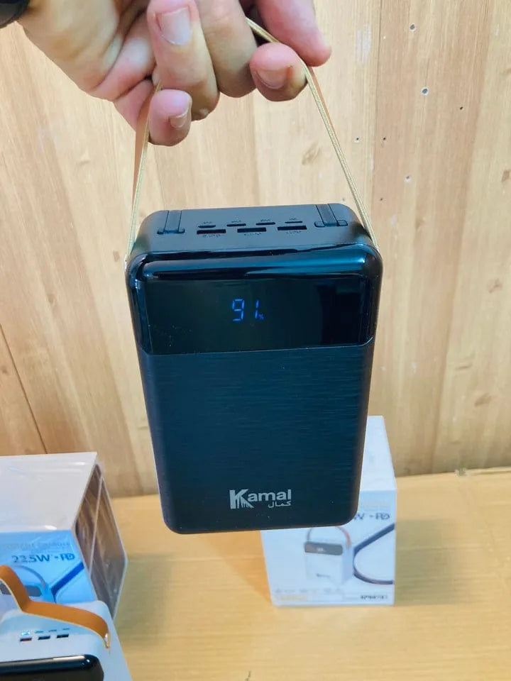 Black power bank with digital display held by a hand on a wooden surface